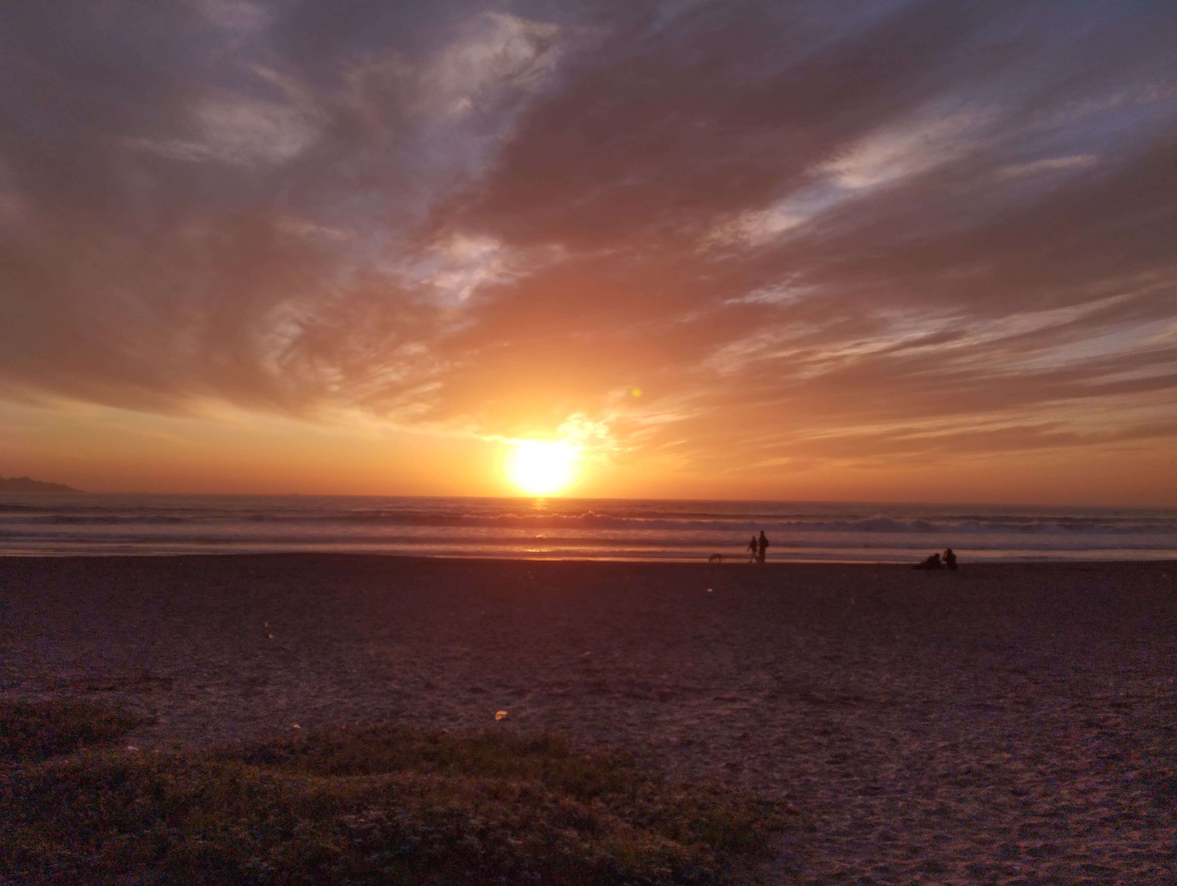 Atardecer en la playa de La Serena con el sol descendiendo sobre el mar y personas caminando por la orilla