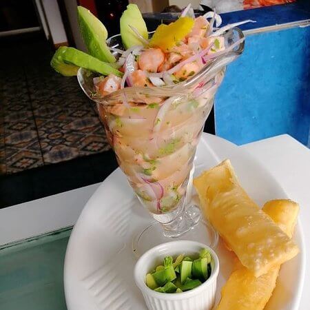 <img src="ceviche.jpg" alt="Copa de ceviche de mariscos con cebolla morada y palta, acompañada de yuca frita y ají verde">