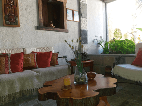 Sala de estar interior con sillones blancos, cojines rojos y mesa rústica de madera en el Hostal Balmaceda